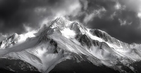 Snow-covered mountain peaks under dramatic cloudy sky with dark forest at base creating a moody atmosphere