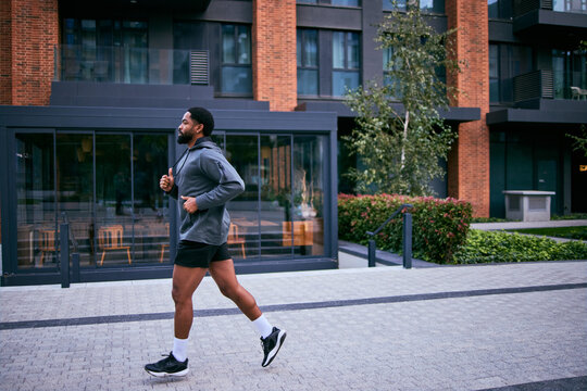 Athletic Man Running Outdoors in Urban Setting Near Modern Brick Building and Glass Facades