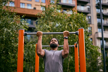 Man Doing Pull-Ups At Outdoor Gym In City Park, Focused On Training And Fitness