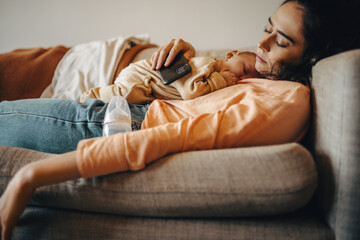 Tired mother and baby resting on sofa with phone