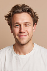 Fototapeta premium A young adult man smiles warmly at the camera. He has medium brown hair and blue eyes. He is wearing a plain white t-shirt. The background is a neutral color.