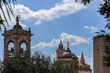 Iconic towers of Bergamo stand framed by trees, showing the cathedral bell tower, Santa Maria...
