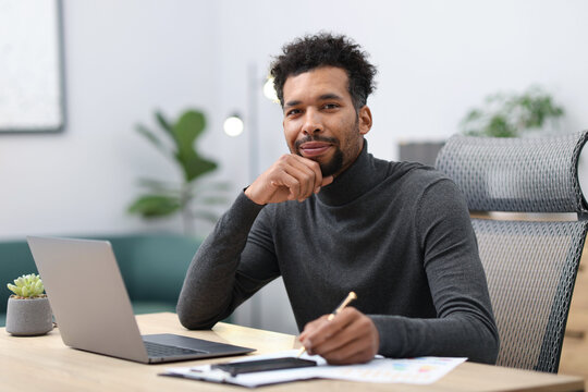 Man working with laptop and writing at table in office