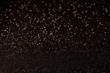Golden glitter scattered on deep black background with sharp focus at bottom, creating dramatic starry effect with shimmering particles for elegant design use