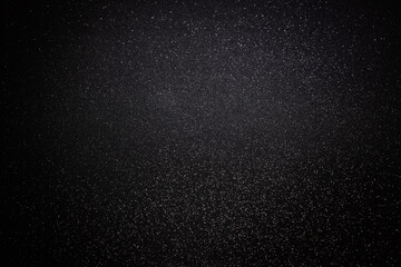 Dark textured surface highlighted above where shimmering grains catch light, offering mysterious celestial backdrop with refined sparkling details for design use