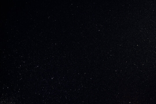 Dark granular surface enriched with glitter and golden inclusions, sharp macro focus highlights rare spark points