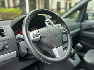 Steering wheel and dashboard showcase the interior of a modern vehicle parked in an urban setting on a bright sunny day