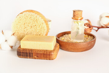 Soap bar, massage brush, sea salt, essential oil and cotton flowers on white background