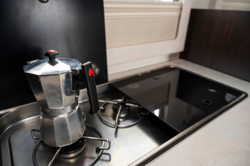 A coffee pot sits on a stove burner. A lighter is next to the coffee pot. The coffee pot is silver and has a red handle