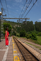 A woman stands on a train platform, looking out over the tracks