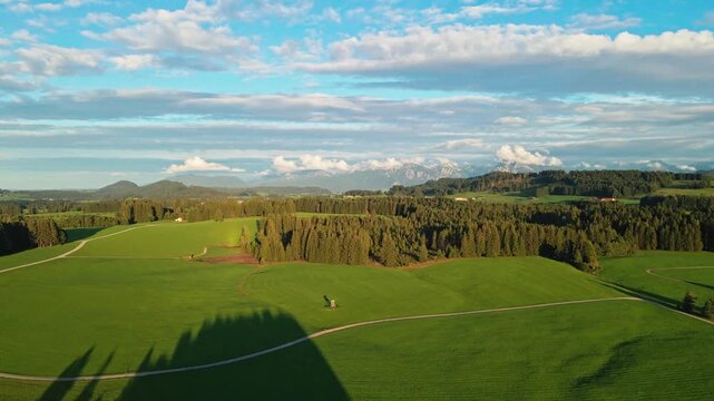 Aerial view of lush green fields and a dense forest under a partly cloudy sky, creating a vibrant contrast of colours, Nesselwang, Bayern, Germany.