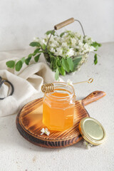 Jar of honey with flowers of acacia and dipper on light background