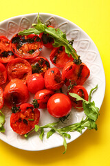 Plate with tasty grilled tomatoes and arugula on yellow background