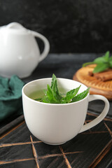 Teapot with cup of fresh mint tea, lemon and cinnamon on grunge black background