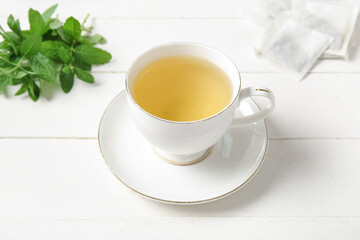 Cup of fresh mint tea on white wooden background