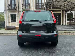 Compact black car parked in front of a vintage building with elegant architecture on a cloudy day