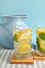 Glasses and jug of infused water with lemon and mint on blue background