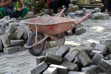 Stacked paving blocks in foreground with worker's torso blurred in background, suggesting active construction work and material readiness.