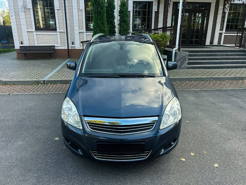 Elegant blue car parked in front of a stylish building with large windows and green trees under a clear blue sky - Powered by Adobe