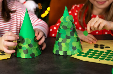 Close up of childrens hands make Christmas tree diy from green paper for Christmas holidays. Little girls create New Year craft