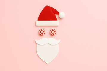 Santa claus face made of hat, candies, and beard on a pink background for holiday celebration, christmas