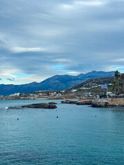 Naklejka premium Scenic coastal view showcasing a tranquil shoreline and mountainous backdrop under a cloudy sky during a calm afternoon in Greece