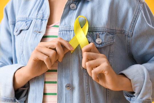 Woman with yellow awareness ribbon on color background, closeup