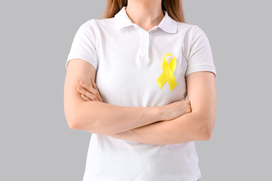 Woman with yellow awareness ribbon on light background, closeup