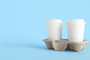 Holder with white takeaway paper cups on blue background