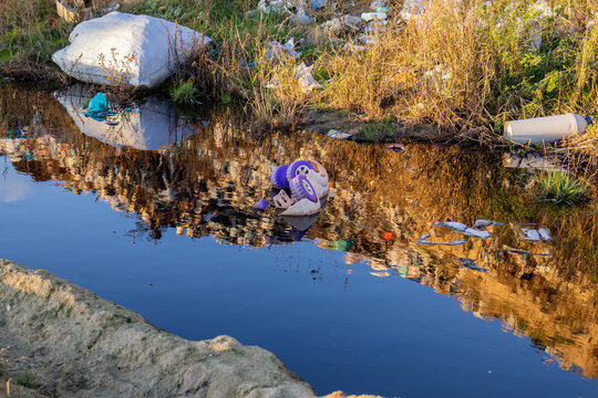 A waterway with dark, polluted water reflects garbage and waste along its banks, highlighting significant environmental issues
