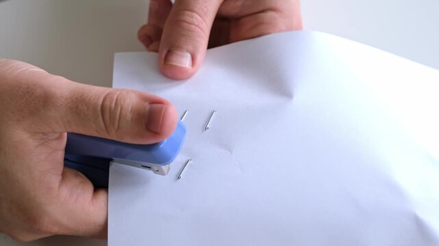 Man stapling sheets of paper with a blue office stapler. Male's hands hold a stapler. Testing of working the stationery. Method of stress relief on workplace. Concept of release negative emotions. 4K.