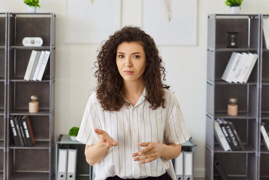Portrait of a young woman standing in office having online webinar or video call with colleague or a friend. Confident pretty company employee having online business conference. Technology concept.