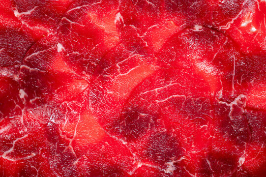 Close-up of raw, thinly sliced red meat with white fat marbling, providing a vibrant food background texture