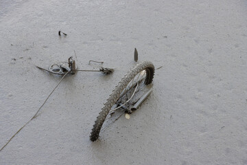 Broken bicycle and wheel in thick brown river mud