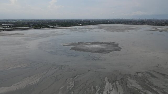Aerial view of the vast, grey mudflow field contrasting with the cityscape in the distance, a somber landscape, Yogyakarta, Yogyakarta, Indonesia.