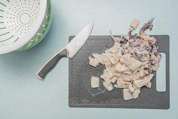 The asymmetrical arrangement of the squid pieces on the gray Teflon creates a dynamic composition, showcasing the different cutting angles and natural shapes