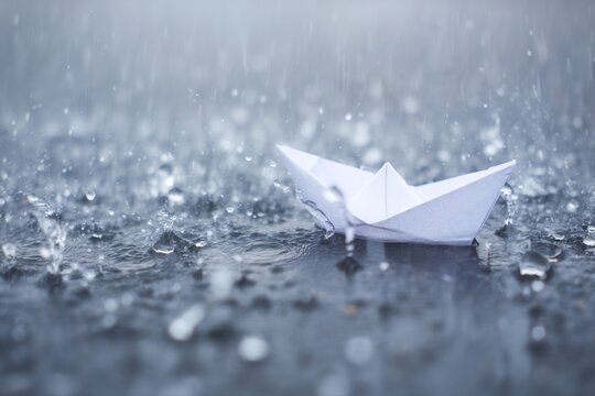 A delicate paper boat floats on a rain-drenched surface, embodying serene hope and quiet resilience amidst gentle downpours, a symbol of life's contemplative journeys