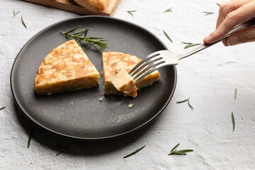 Female hand eating Spanish potato omelette tortilla served on black dish 