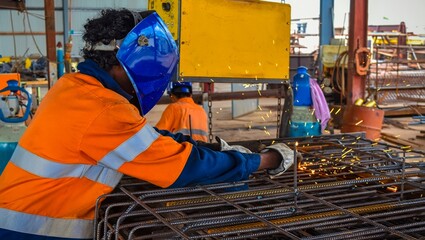 Skilled welder in protective gear meticulously joins steel rebar with bright sparks flying in a fabrication workshop