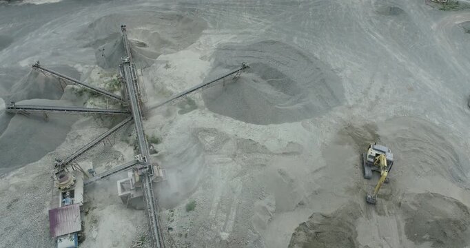 Aerial view of a vast quarry showing intricate conveyor belts and piles of grey stone, contrasting with the surrounding greenery, Palu, Central Sulawesi, Indonesia.