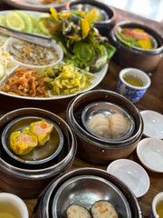 Assorted Dim Sum in Bamboo Steamers with Fresh Vegetables and pickles on a table in restaurant close up