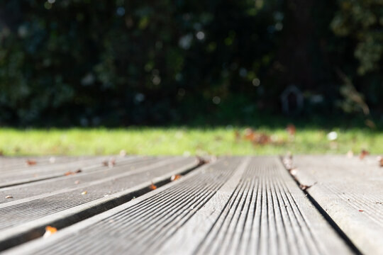 Plan rapproch&eacute; d'un plancher en bois d'une terrasse avec jardin flou en arri&egrave;re plan, format horizontal