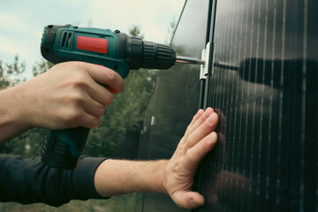 Worker fixing a solar panel. Hands using a cordless drill and mounting bracket.