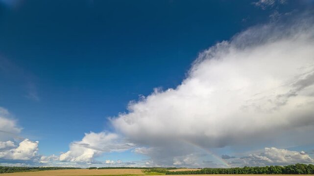 A stunning, majestic cloudscape and rainbow beautifully graces the serene and peaceful landscape below