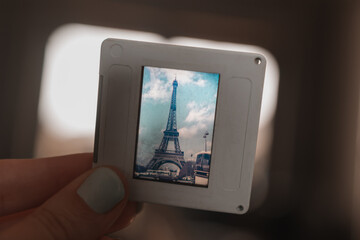 Hand holding a nostalgic film slide featuring the iconic Eiffel Tower in Paris, representing classic travel memories and the analog era of photography
