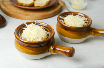 The process of cooking French onion soup. Two ceramic bowls with soup and grated cheese. Traditional cuisine concept. Horizontal orientation. Selective focus.