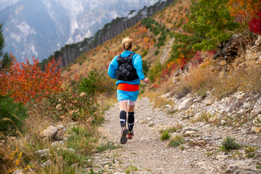 Back view female athlete running mountain marathon in autumn