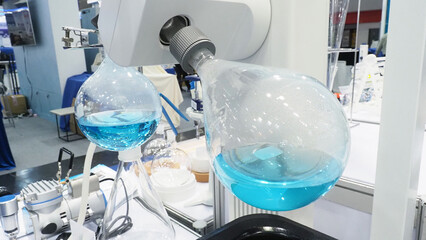 A laboratory rotary evaporator setup with large round-bottom flasks containing blue liquid.