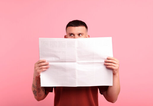 Young man reading newspaper against pink background