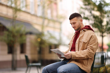 Fototapeta premium Young man reading newspaper on chair outdoors. Space for text